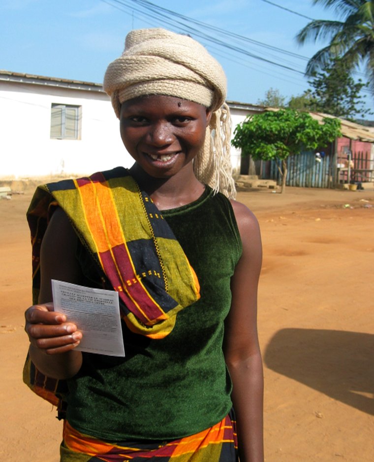 A young woman in Ghana smiling, holding a gospel tract she has just been given