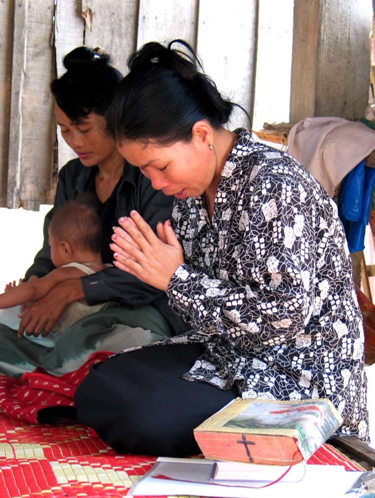 Two women and a small child kneeling in prayer, an open Bible in front of them