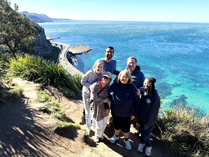The team standing together on a clifftop above the turquoise sea in Australia.