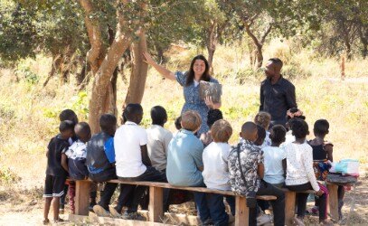 Zambian children seated on benches under the trees for a class.